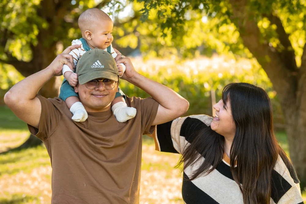 A baby riding on dad’s shoulders while mom looks up during a fall family session.