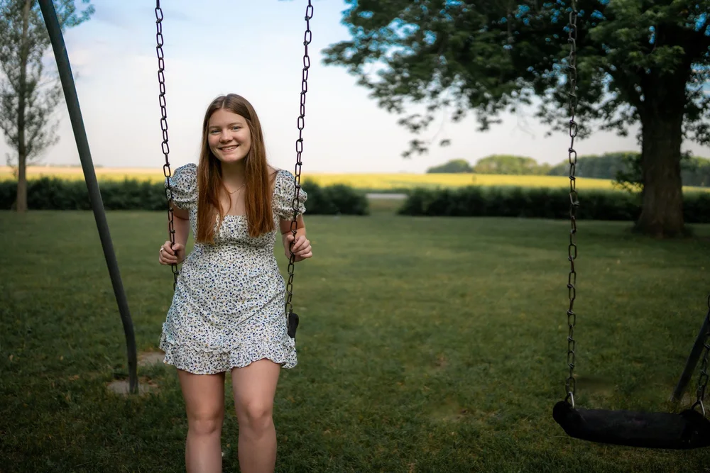 Bella standing in a floral dress and holding the chains of a garden swing.