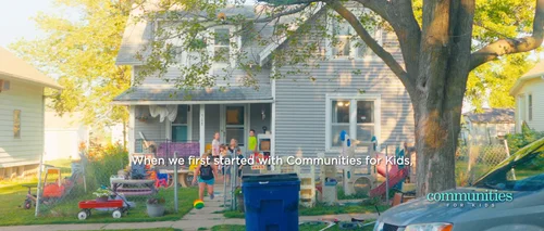 Wide view of a Wausa childcare yard with children, adults, outdoor toys and a large shade tree.