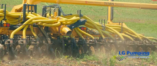 Close view of yellow manure application hoses and metal discs working through soil, with dust rising around the equipment.