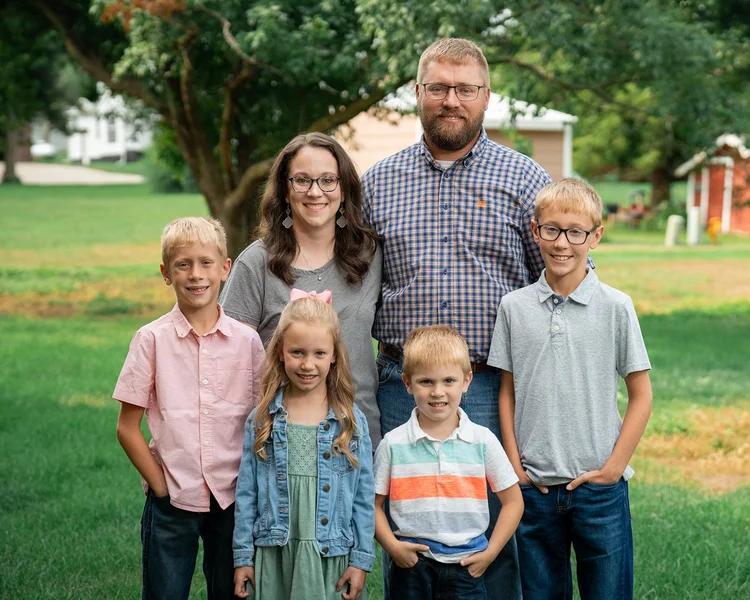 The Jensen parents and four children smiling during an outdoor family portrait.