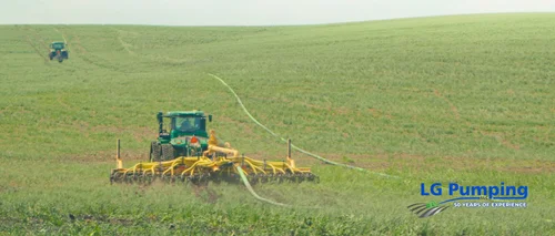 Elevated view of a John Deere tractor and yellow manure applicator working a green field, with a long hose trailing behind.