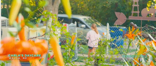 Garden flowers and play equipment outside Carla's daycare in Wausa, with a child in the background.