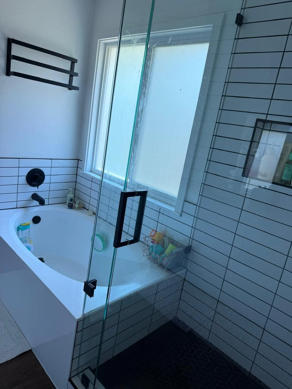 Before: glass shower door with water spots beside a soaking tub in an Austin bathroom
