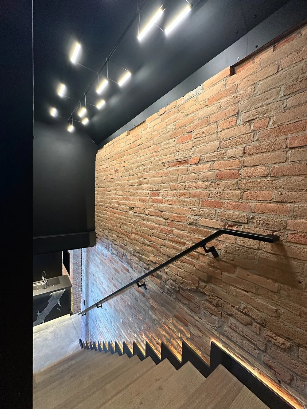 Floating steel stair along a lit brick wall
