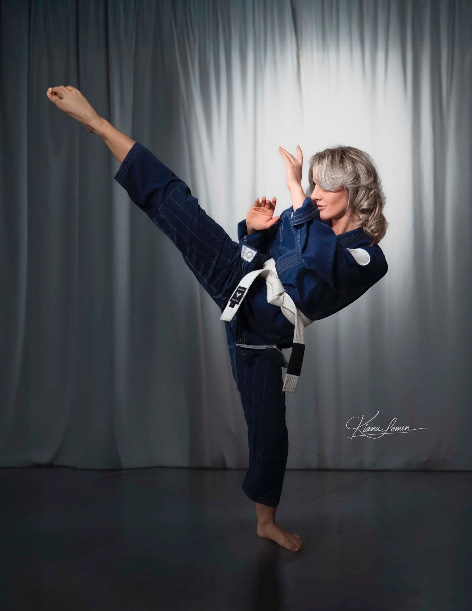Studio portrait of a martial artist performing a high kick in a blue gi