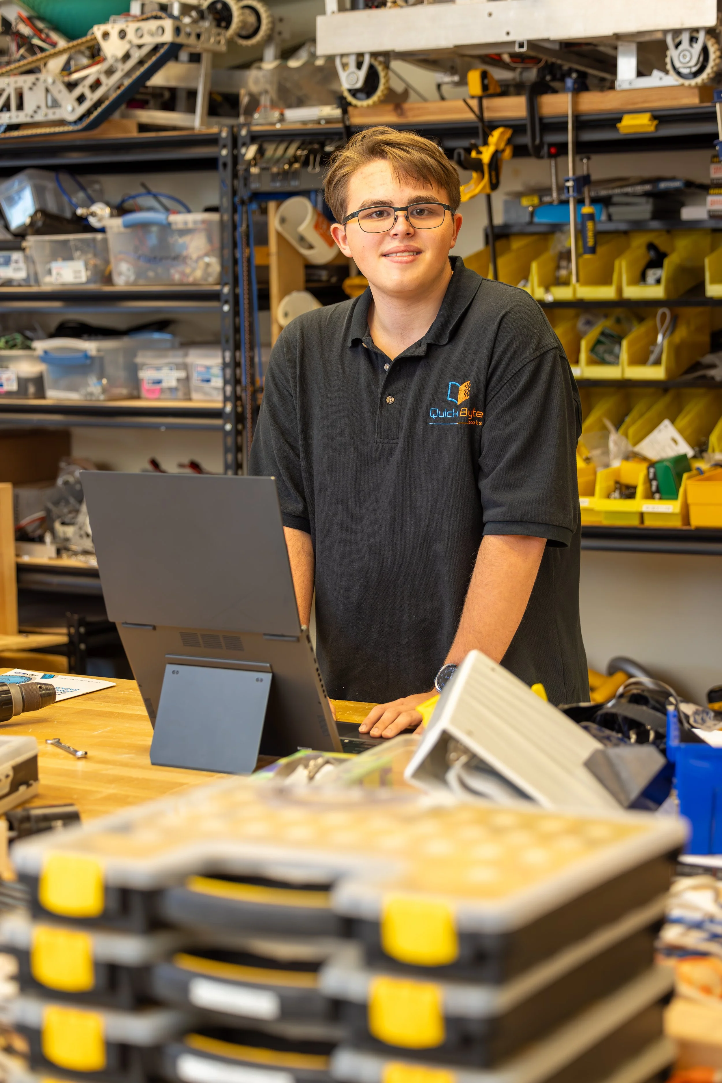 Connor Secrist in a Quick Byte Books polo standing at a laptop in his school's robotics workshop