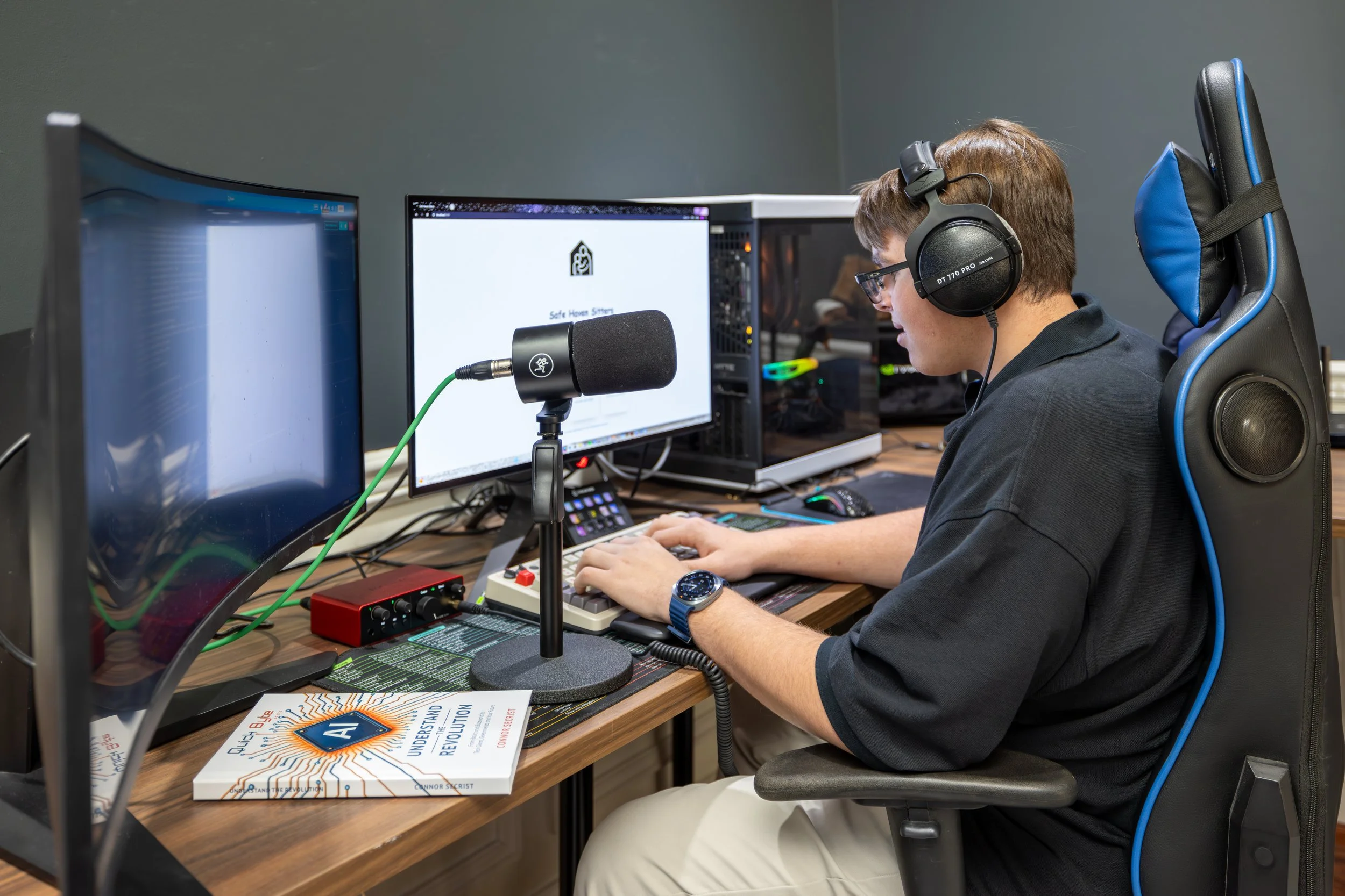 Connor Secrist wearing headphones at his desk with a microphone, his book on the desk beside him