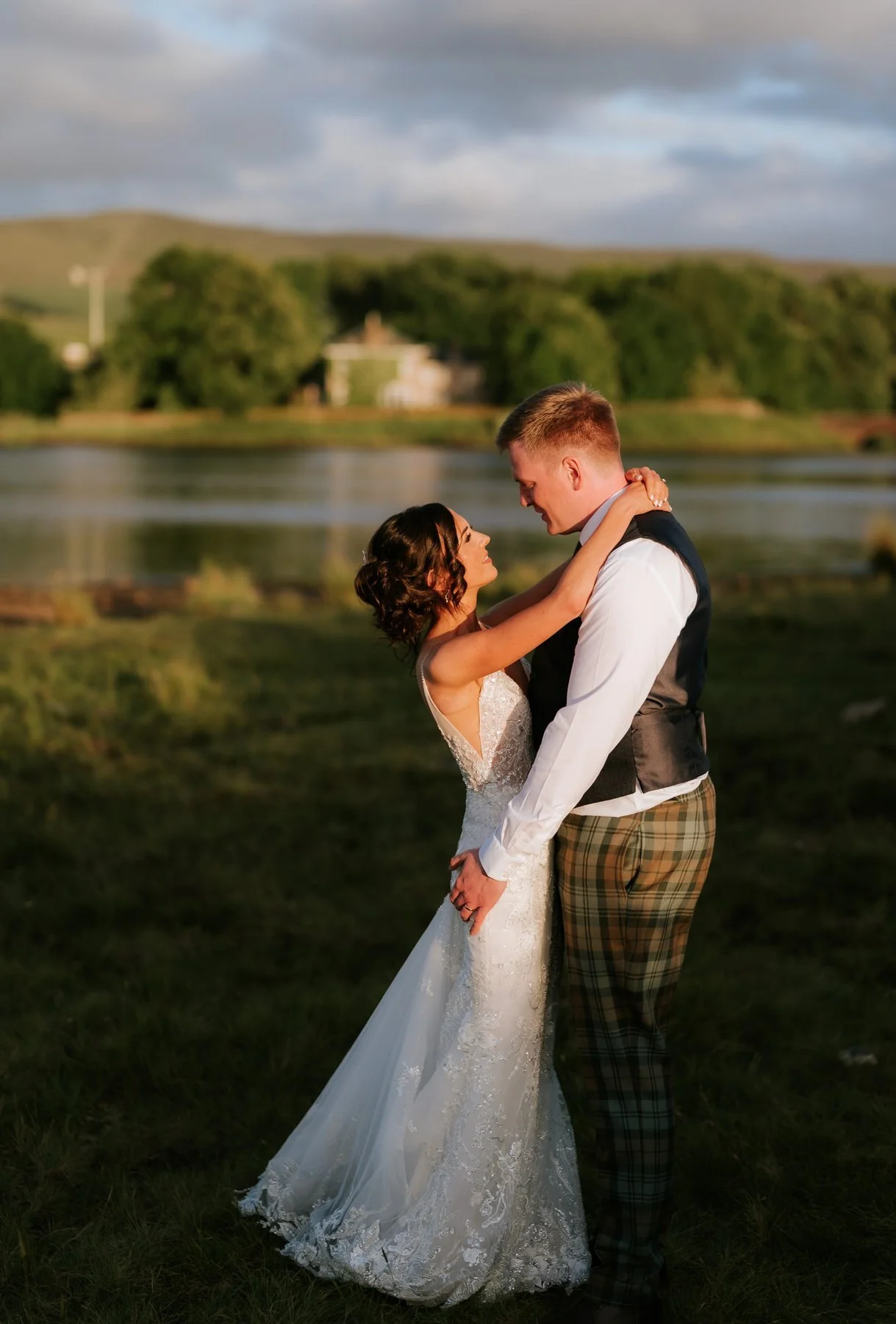 Lauren and Jamie embracing beside the reservoir in warm evening light.