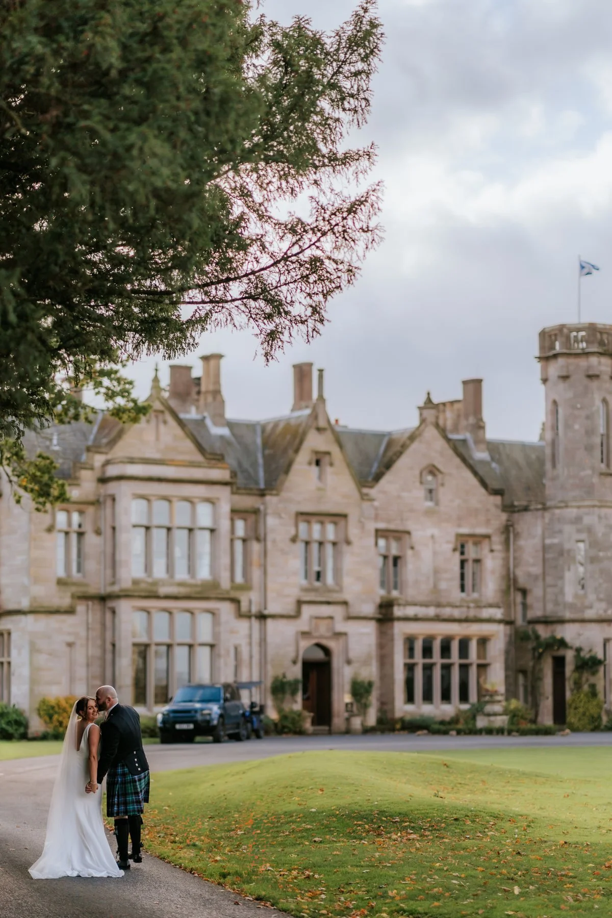 Kendall and Ewen beneath autumn trees with SCHLOSS Roxburghe behind them.