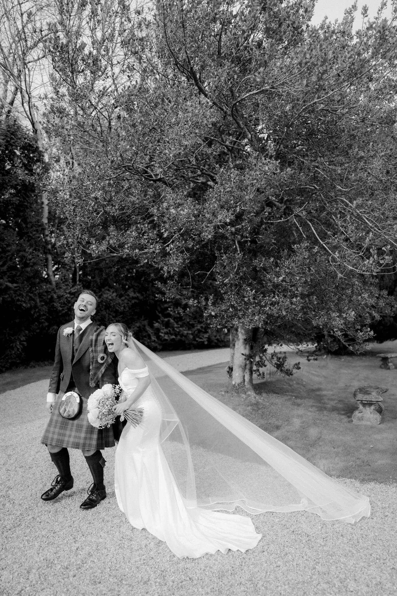 Black-and-white portrait of Elle and Adam laughing beneath a tree