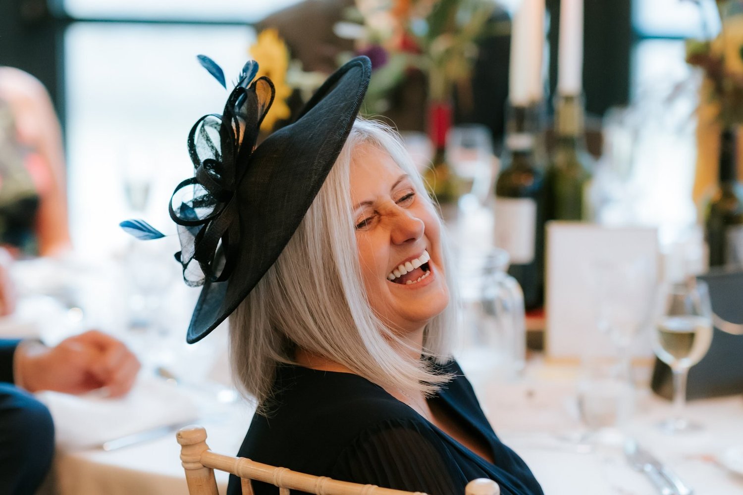 A guest in a dark hat laughing at the wedding breakfast table.