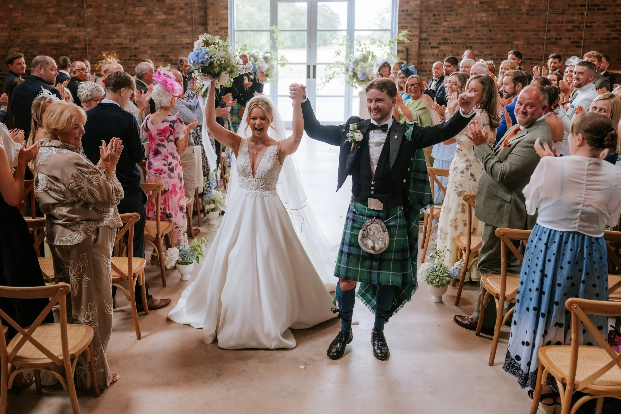 Lilian and Luke raising their arms as guests cheer them back up the aisle.