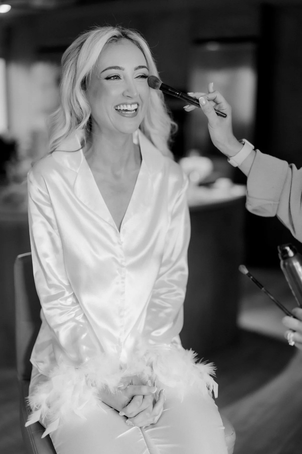 Black-and-white photograph of Lauren laughing while her make-up is finished.