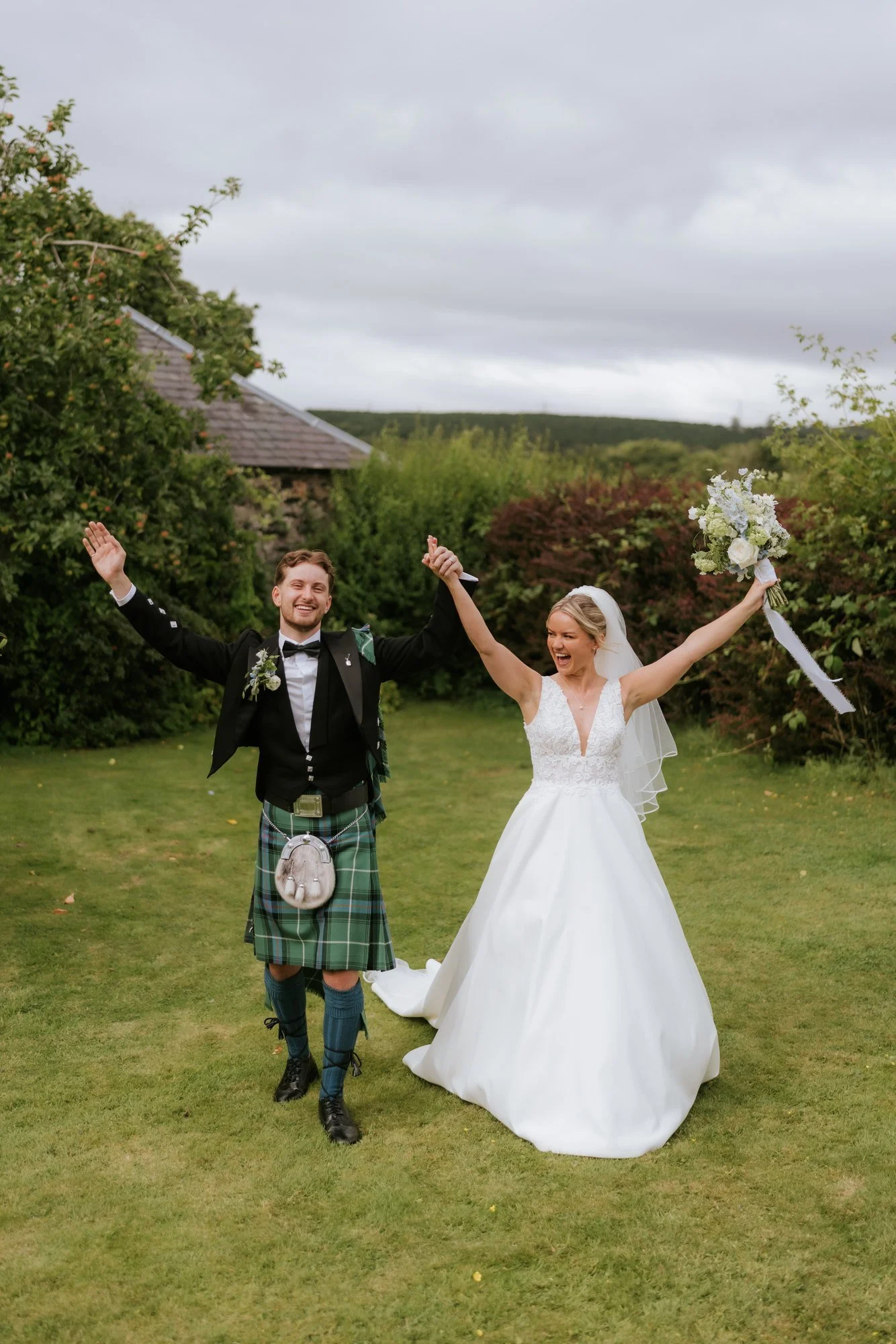 Lilian and Luke laughing with their arms raised after their wedding portraits.