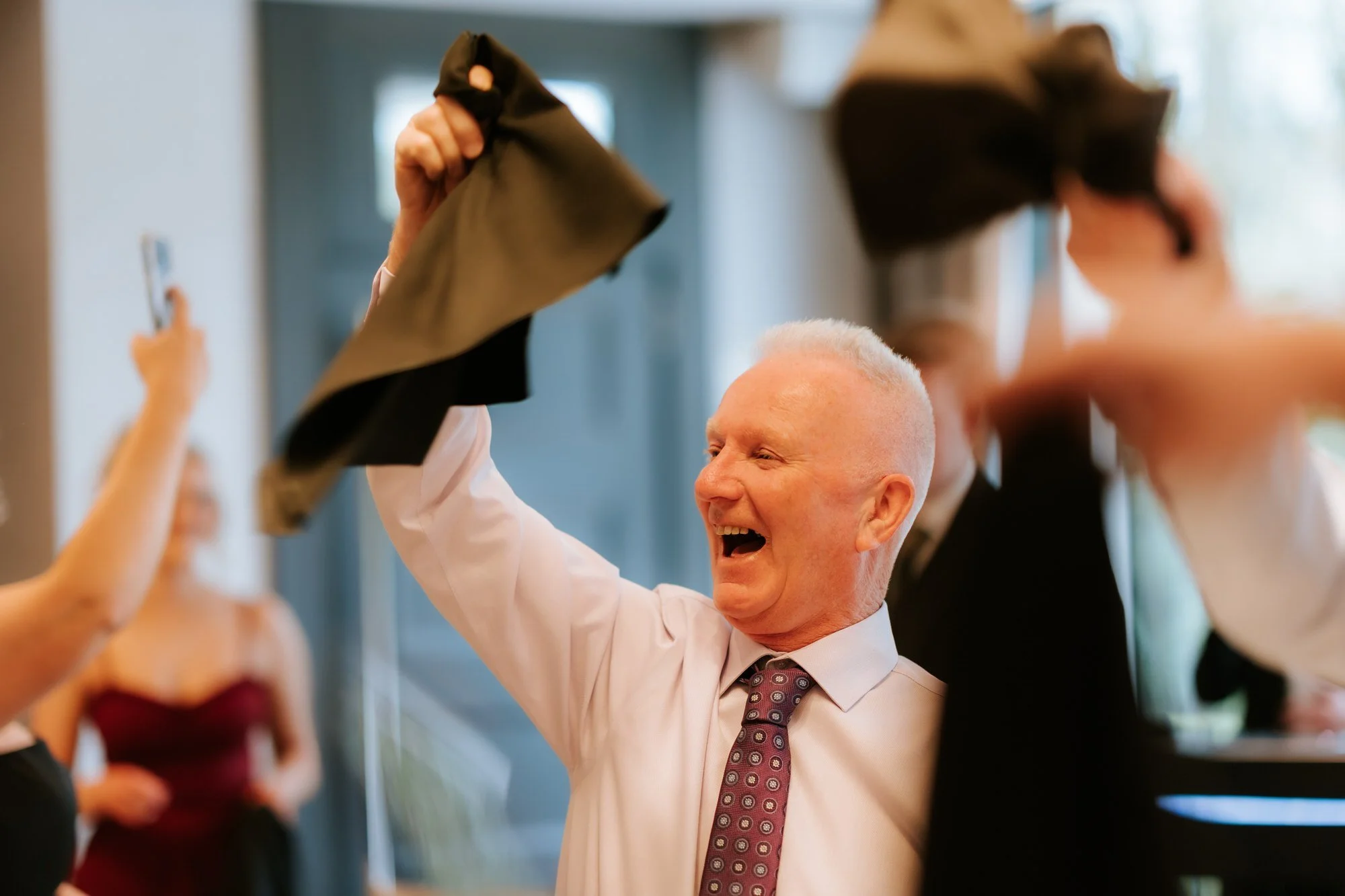 A laughing wedding guest waving a black napkin above his head