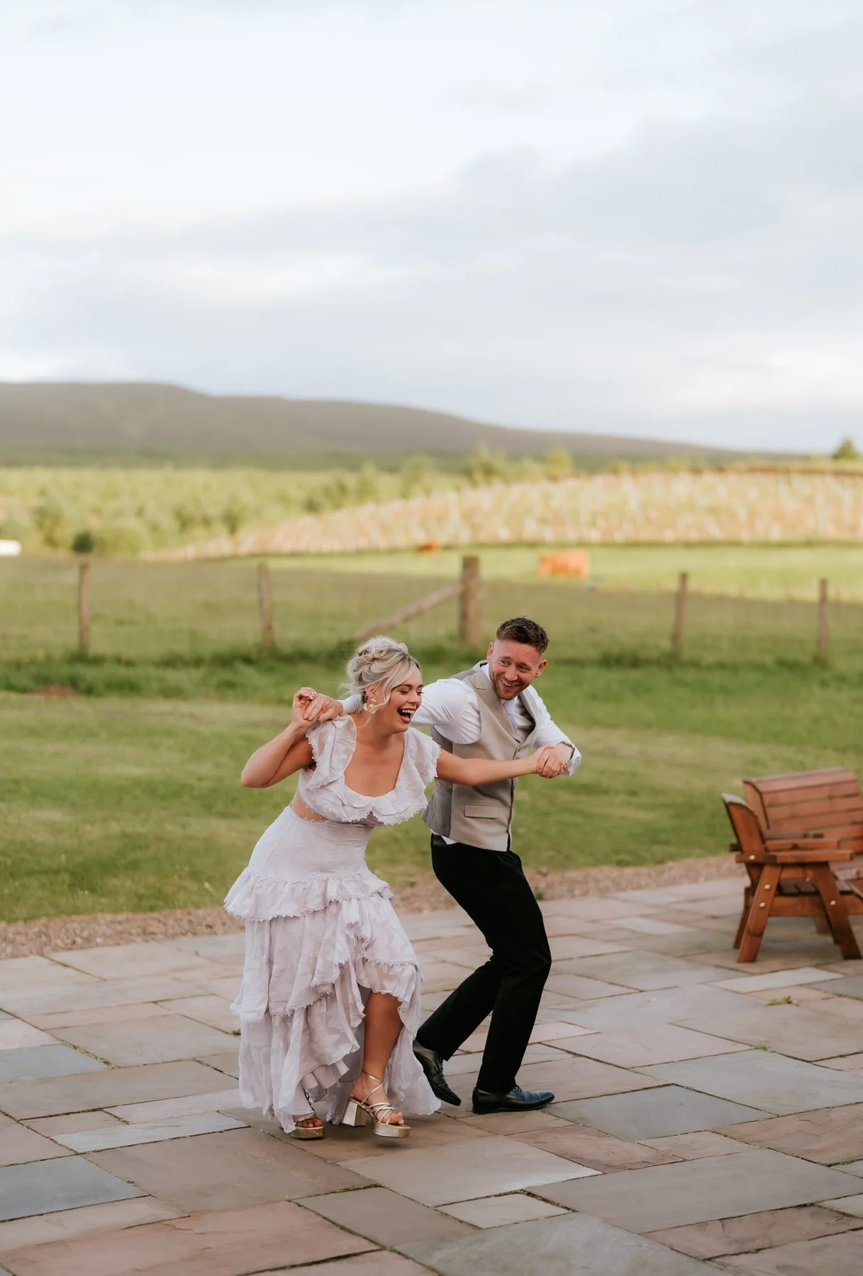 Two wedding guests dancing together on the patio with the Pentland Hills behind them.