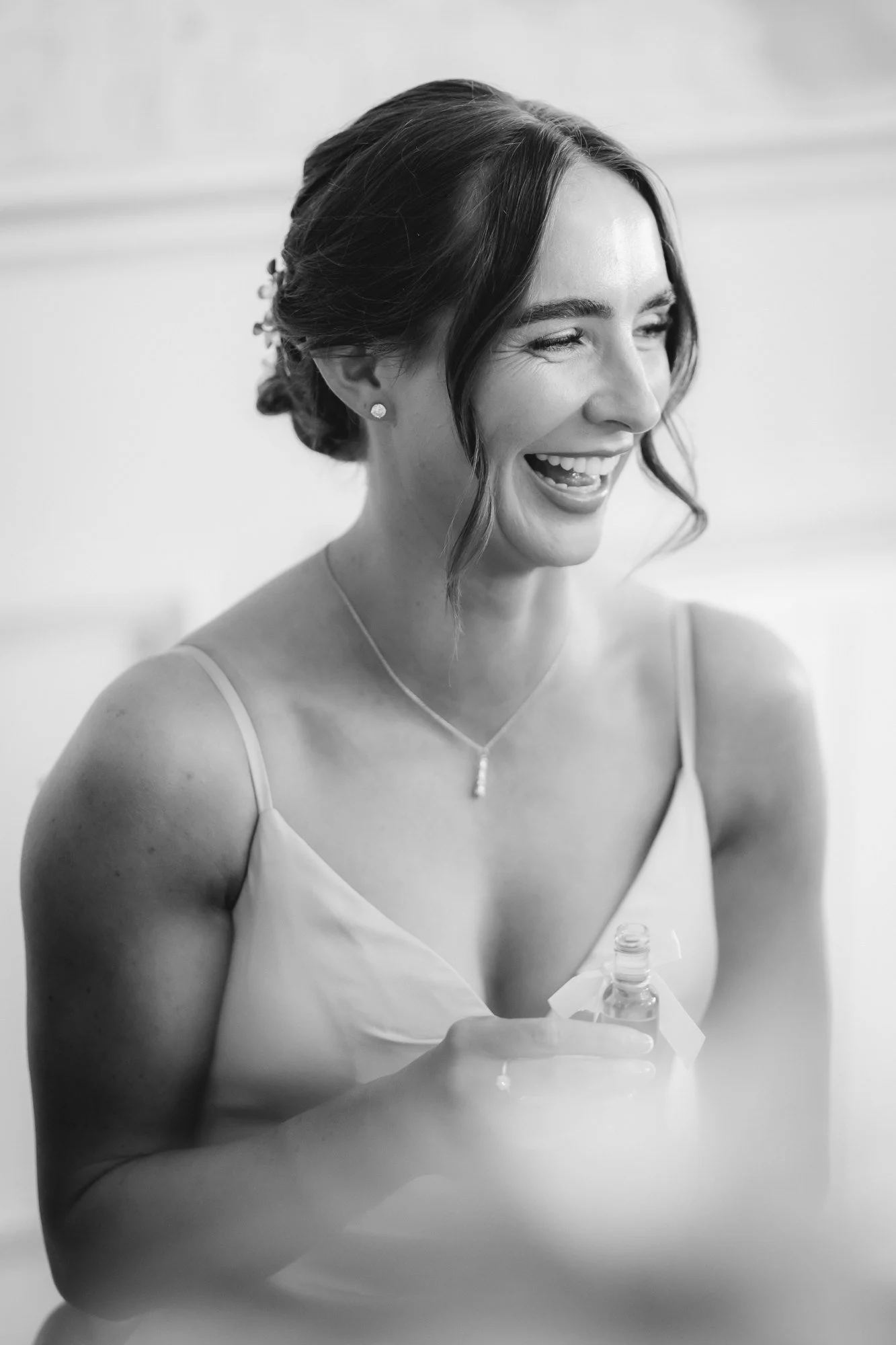 Black-and-white portrait of a bridesmaid laughing with a small bottle in her hand at Glenbervie House.