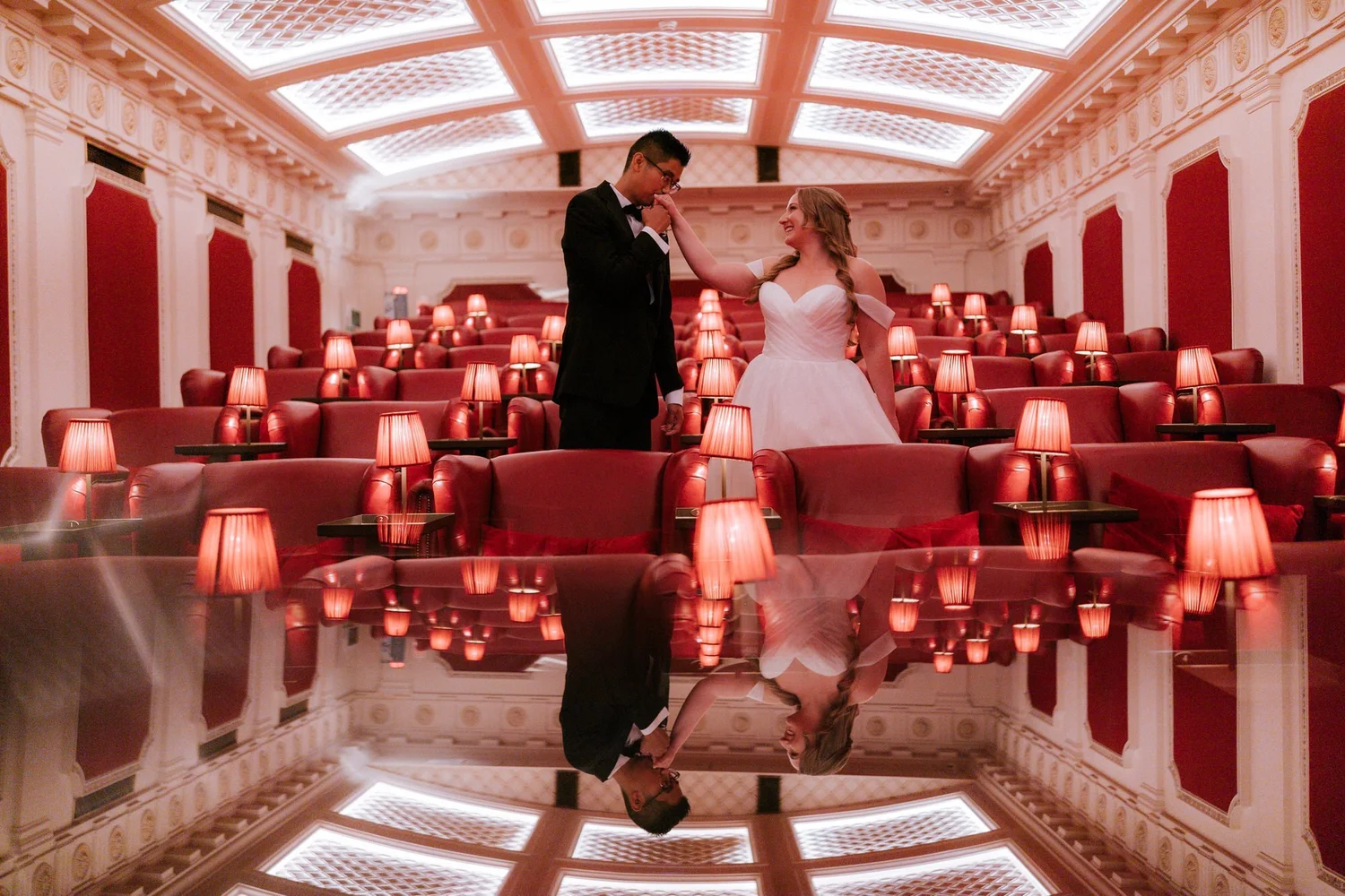 Allie and Carl standing among the red cinema seats at The Scotsman Picturehouse, reflected in a polished table.