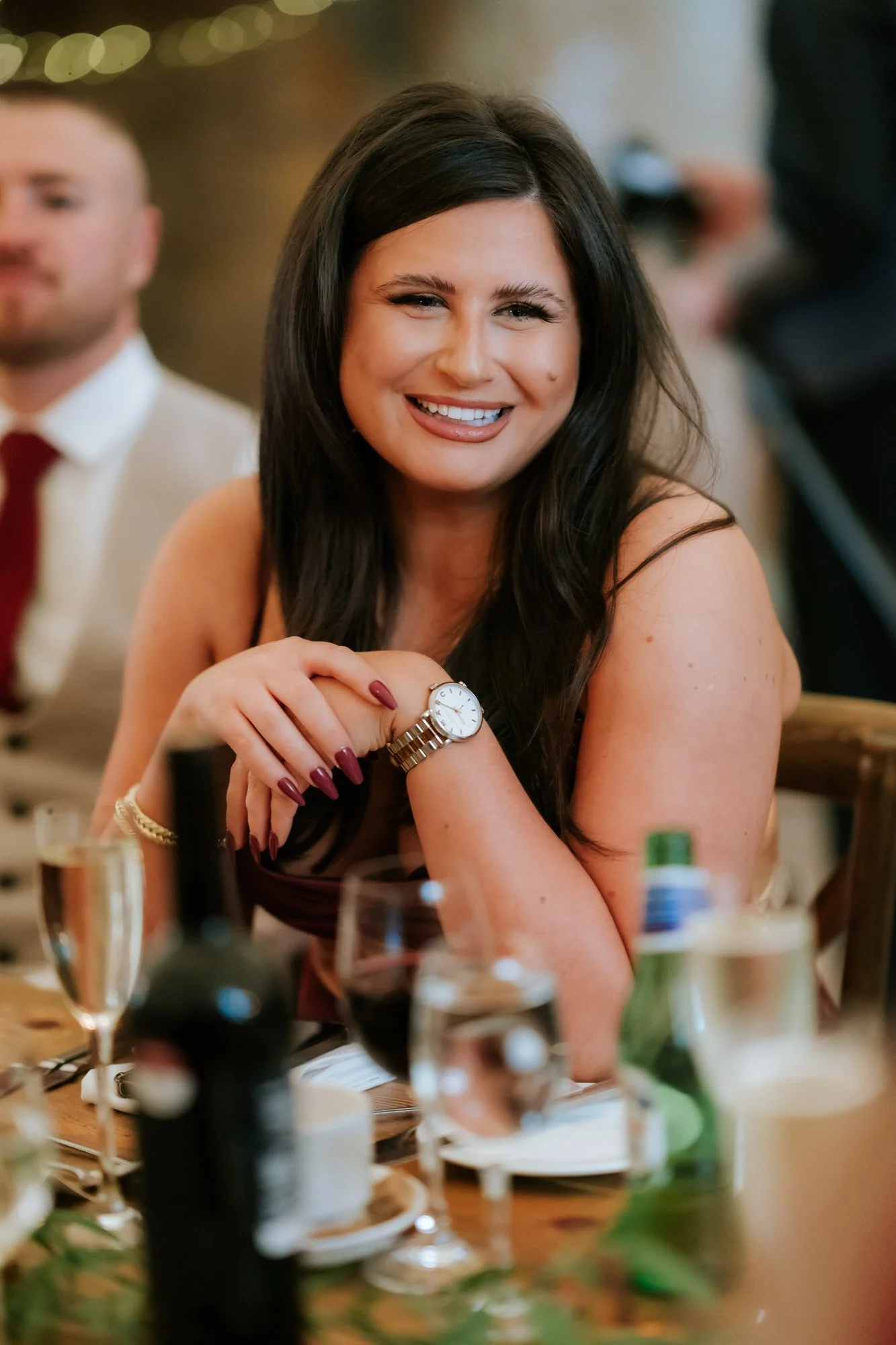 A guest in a navy dress smiles across the table, with her hands resting together.