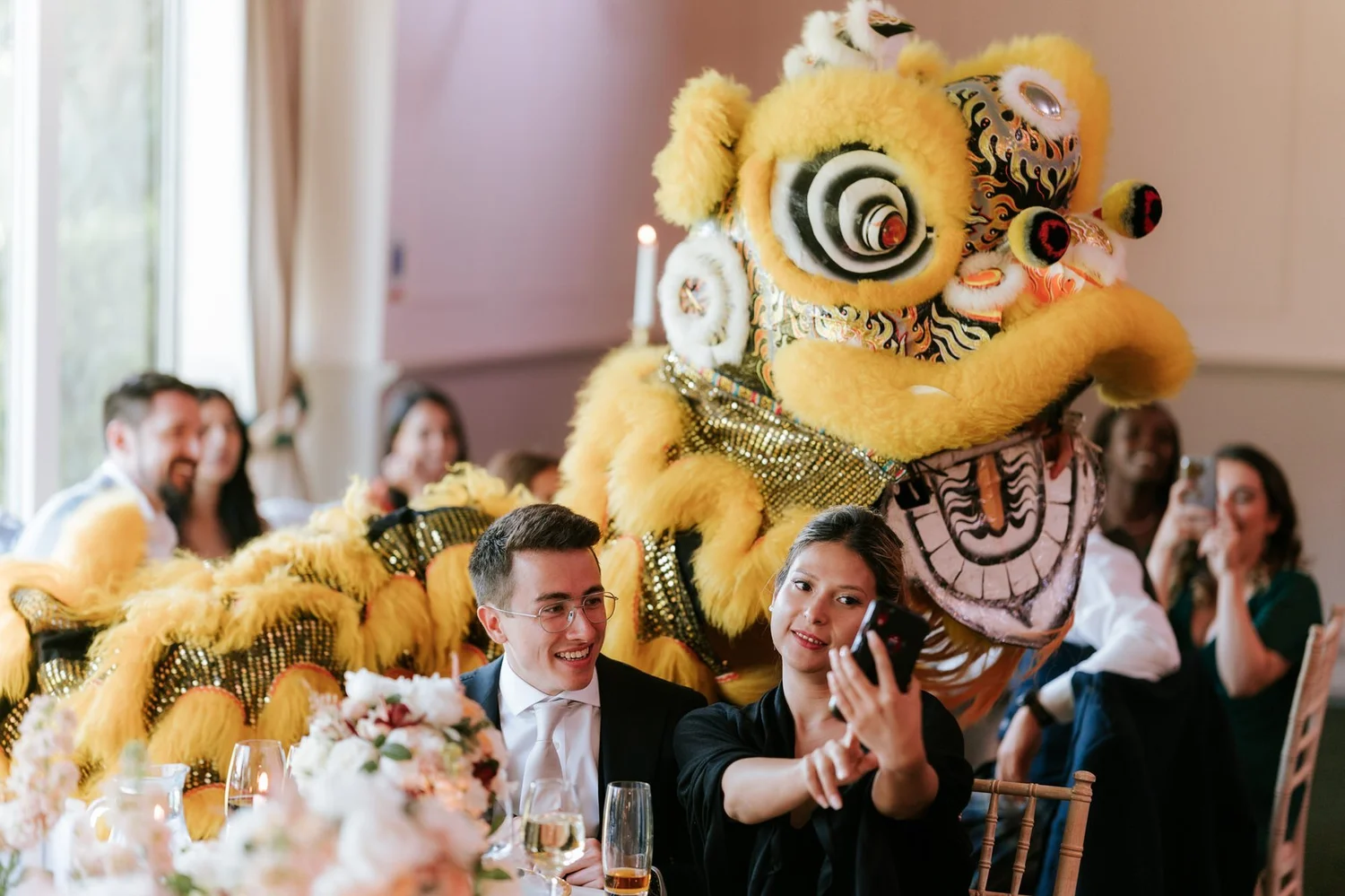 A yellow Chinese lion dancer entertaining guests beside the wedding reception tables.