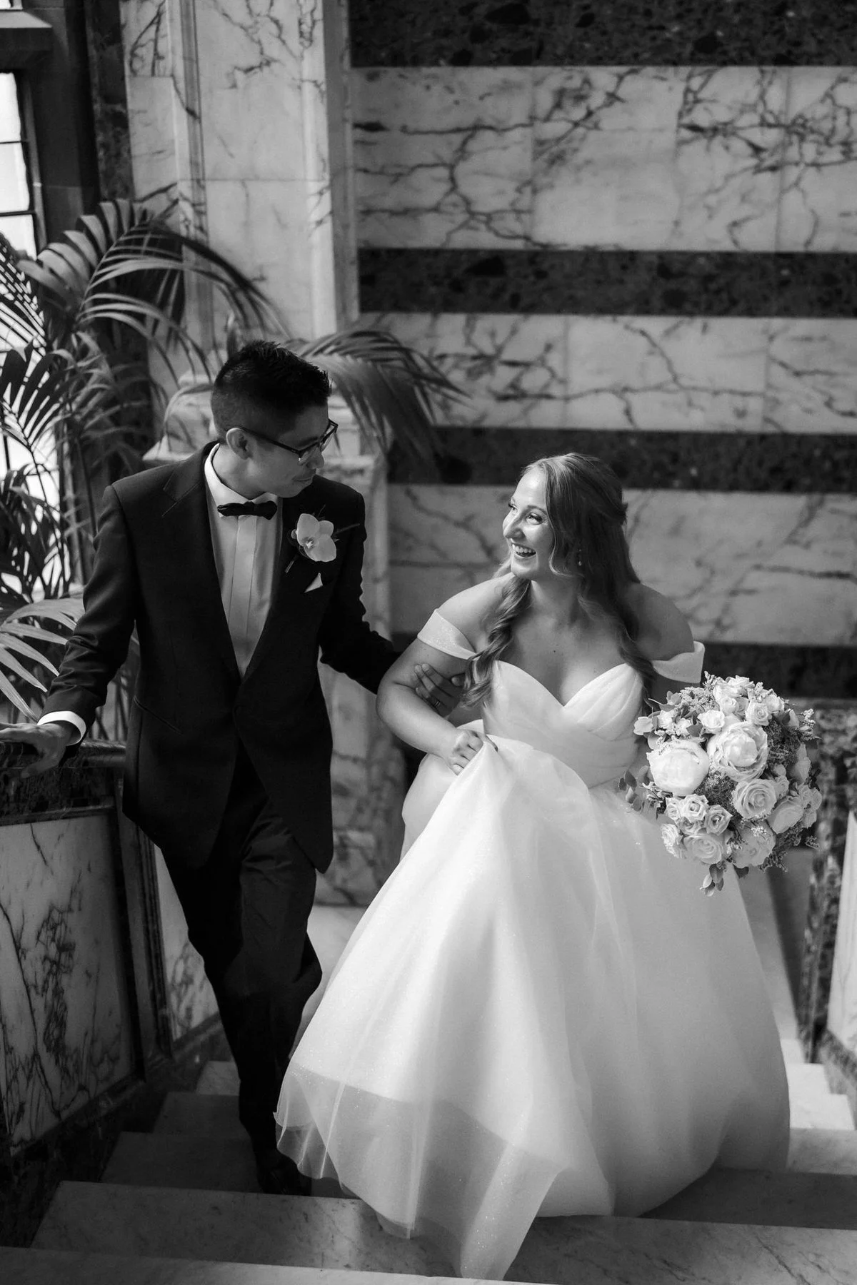 Allie and Carl smiling at one another on the marble stairs, photographed in black and white.