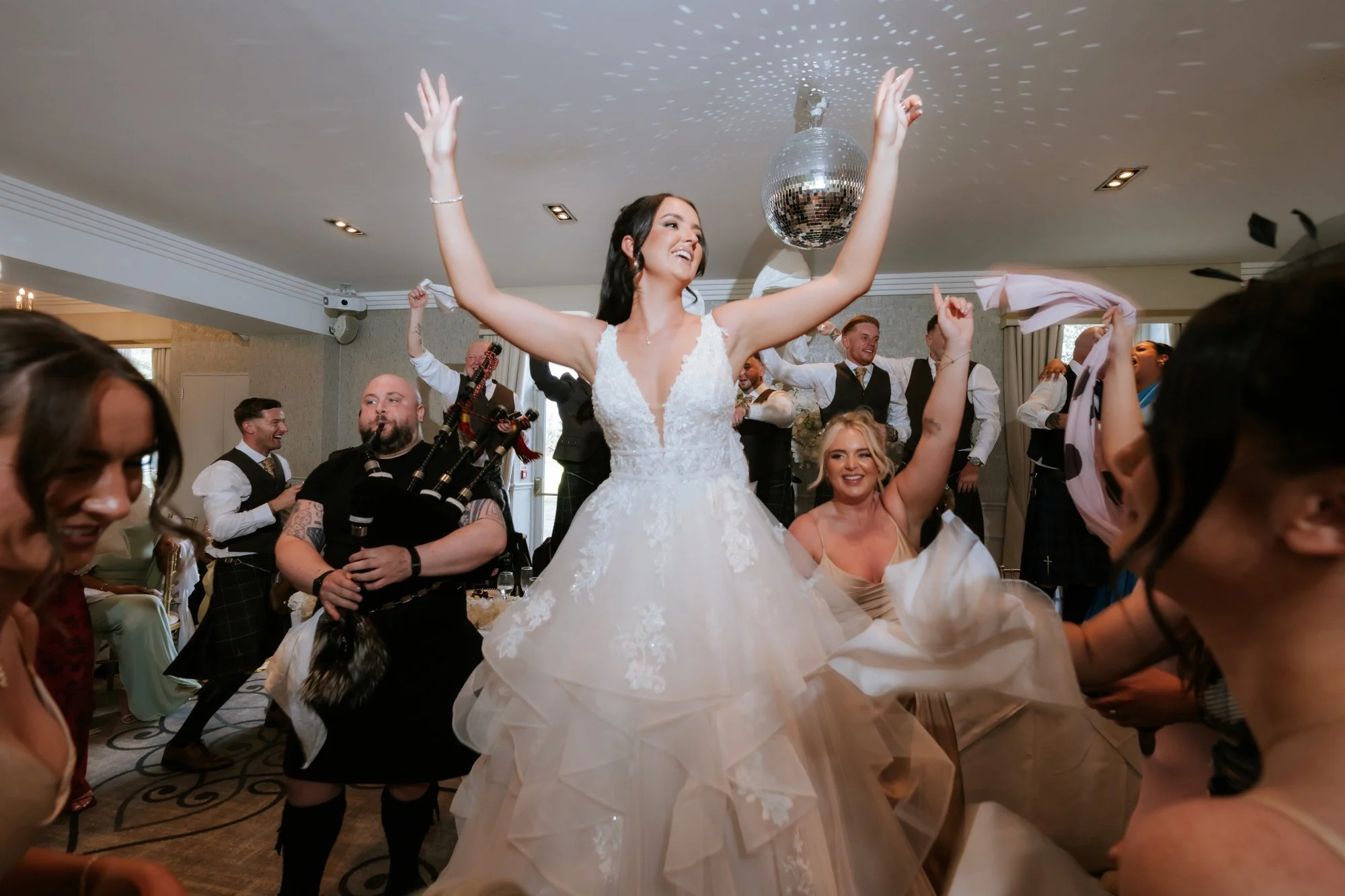 Kaitlyn raising her arms beside the bagpiper as guests celebrate at Glenbervie House.