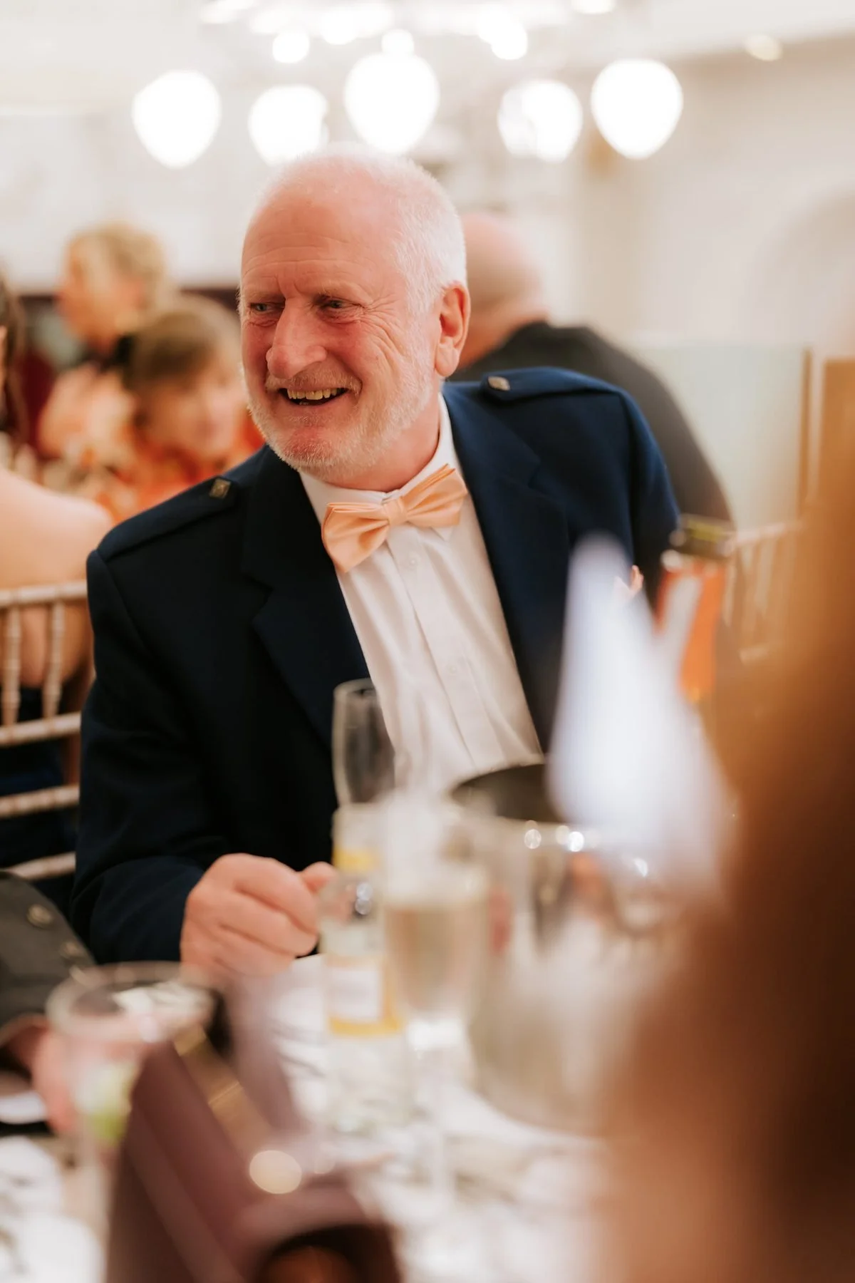 A guest in a navy jacket laughing with friends at the reception.