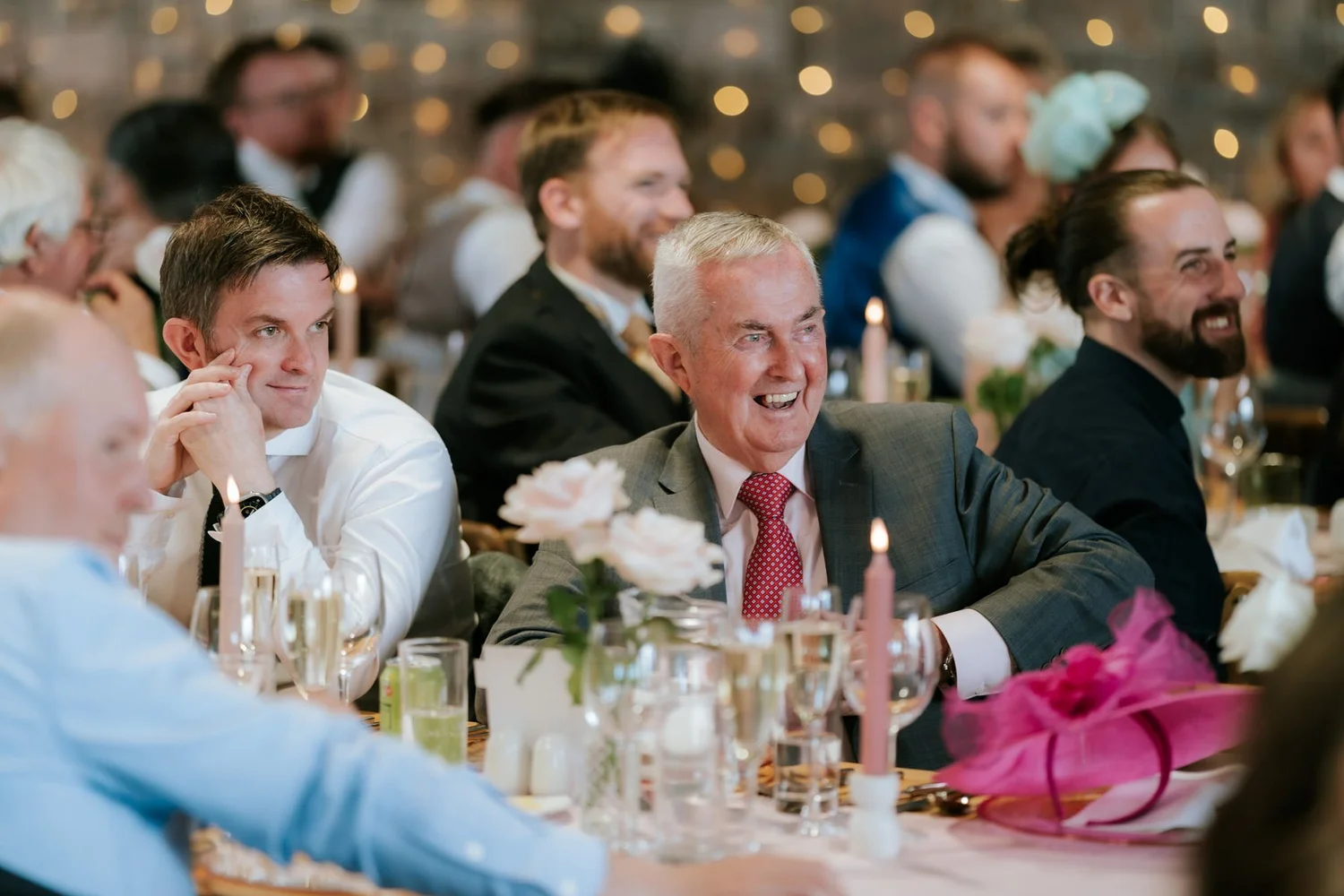 Wedding guests leaning forward and laughing together around their table.