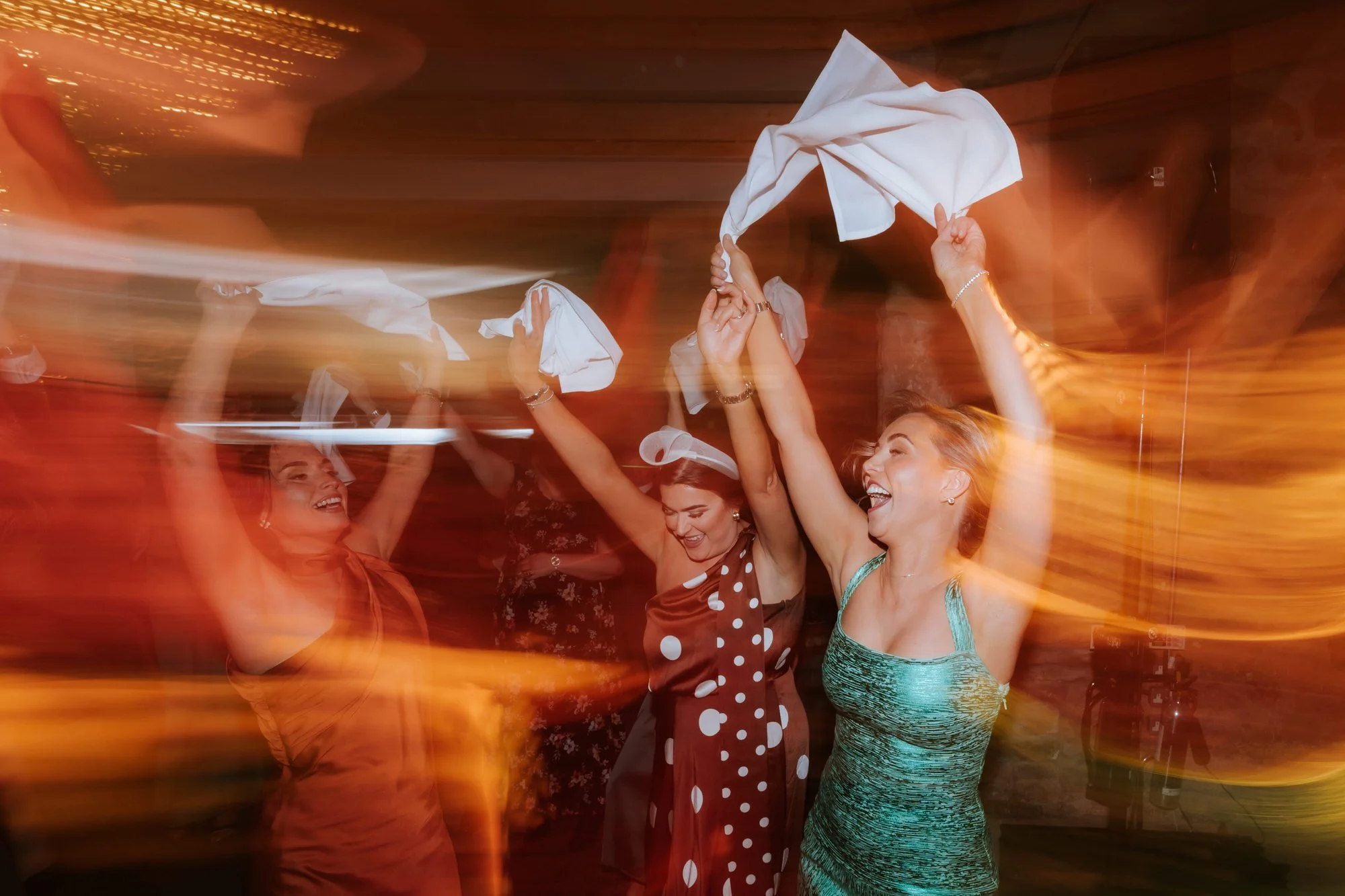 Guests waving white napkins beneath streaks of orange party lighting