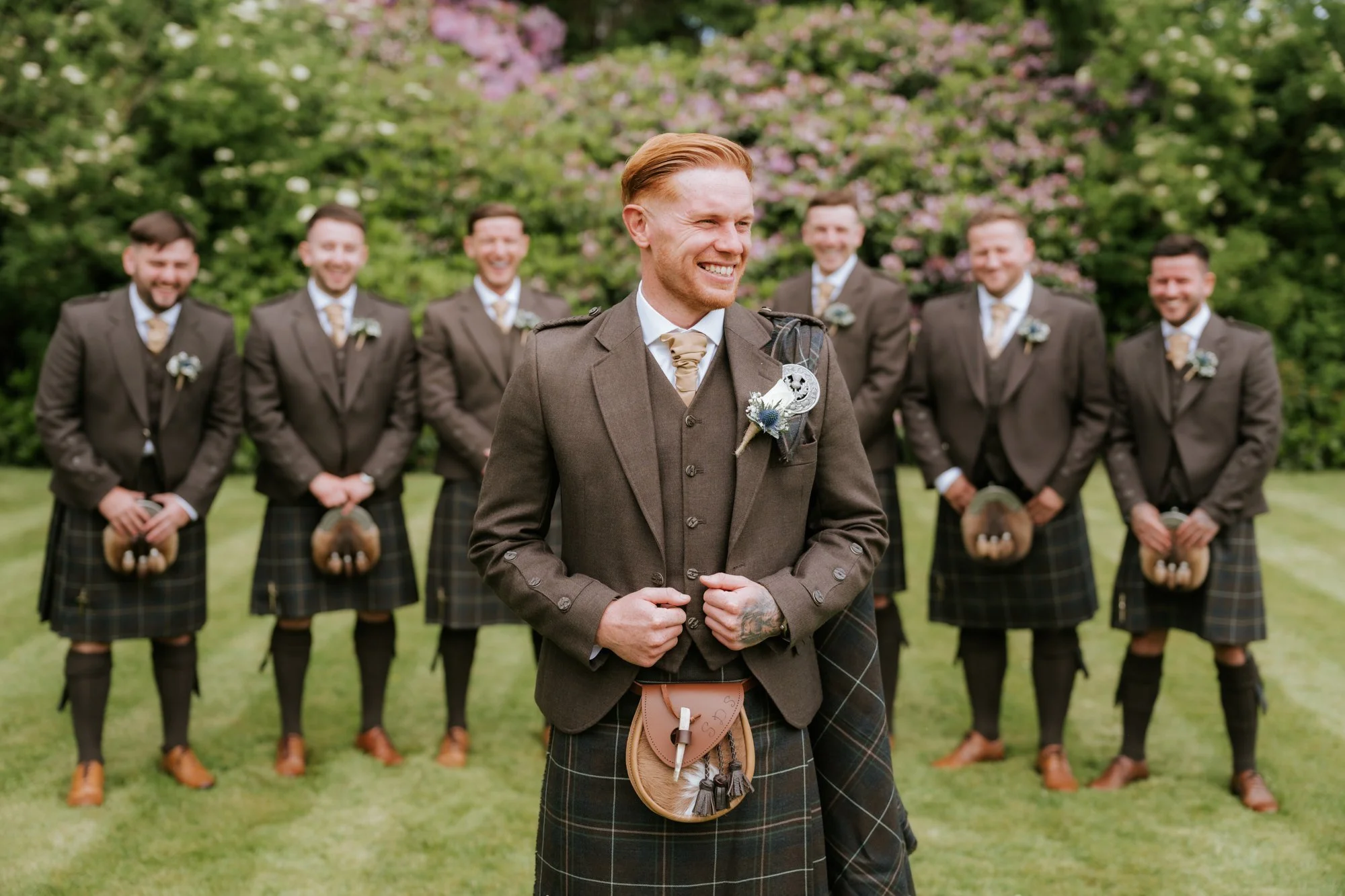Scott smiling with his six groomsmen on the lawn at Glenbervie House.