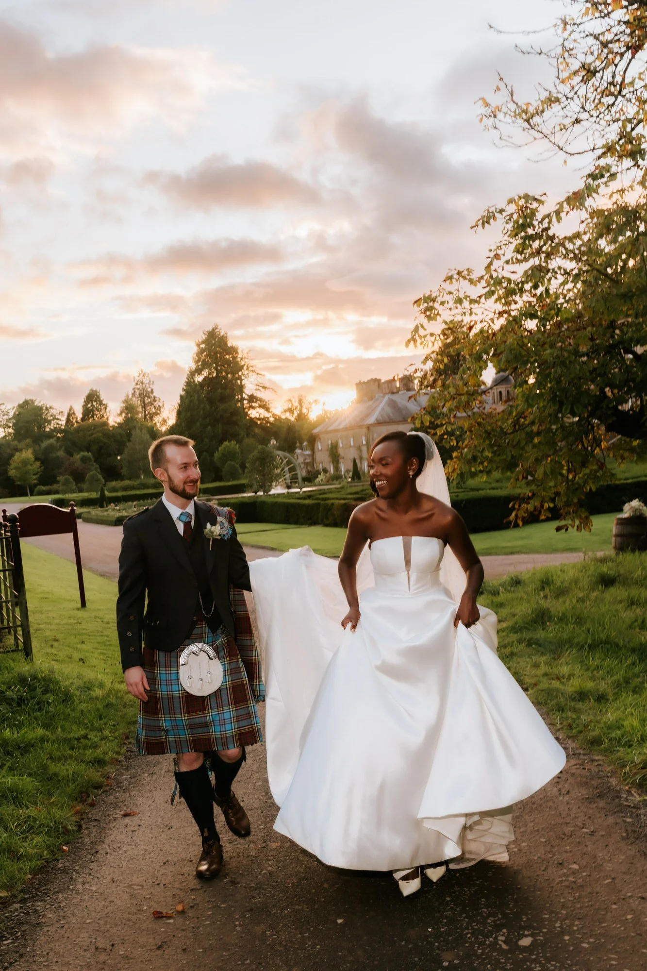 The newlyweds walking along a garden path beneath the sunset sky.