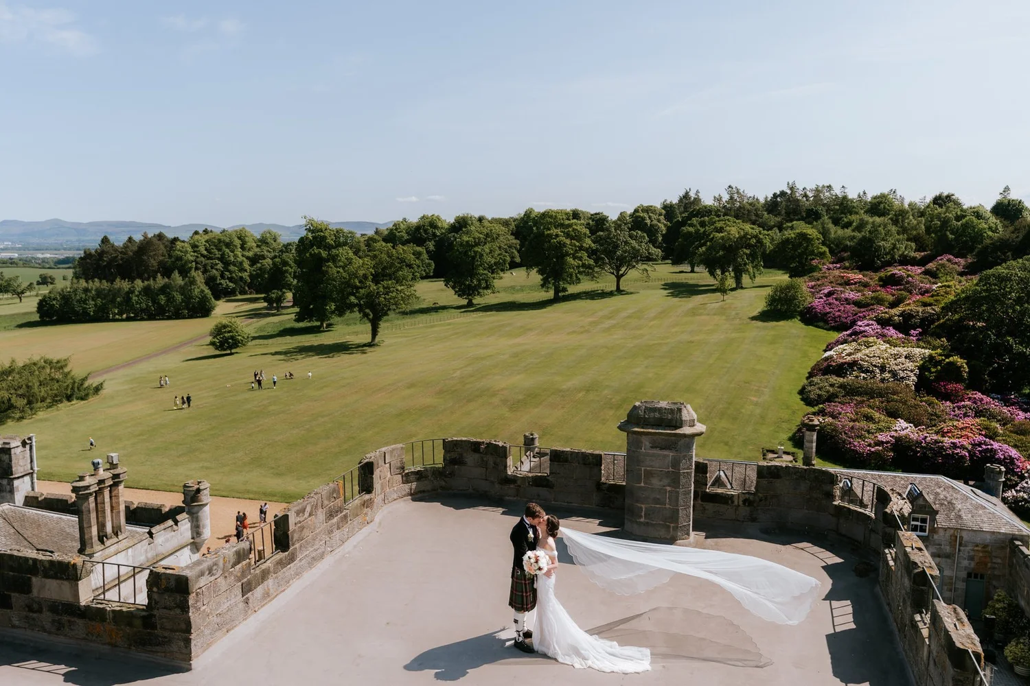 A view from above of Kim and Kenneth on the castle rooftop terrace, with lawns and woodland beyond.