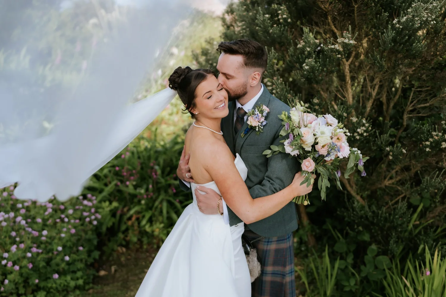 Dougie kissing Lois on the temple as her veil blows across the trees beside them.