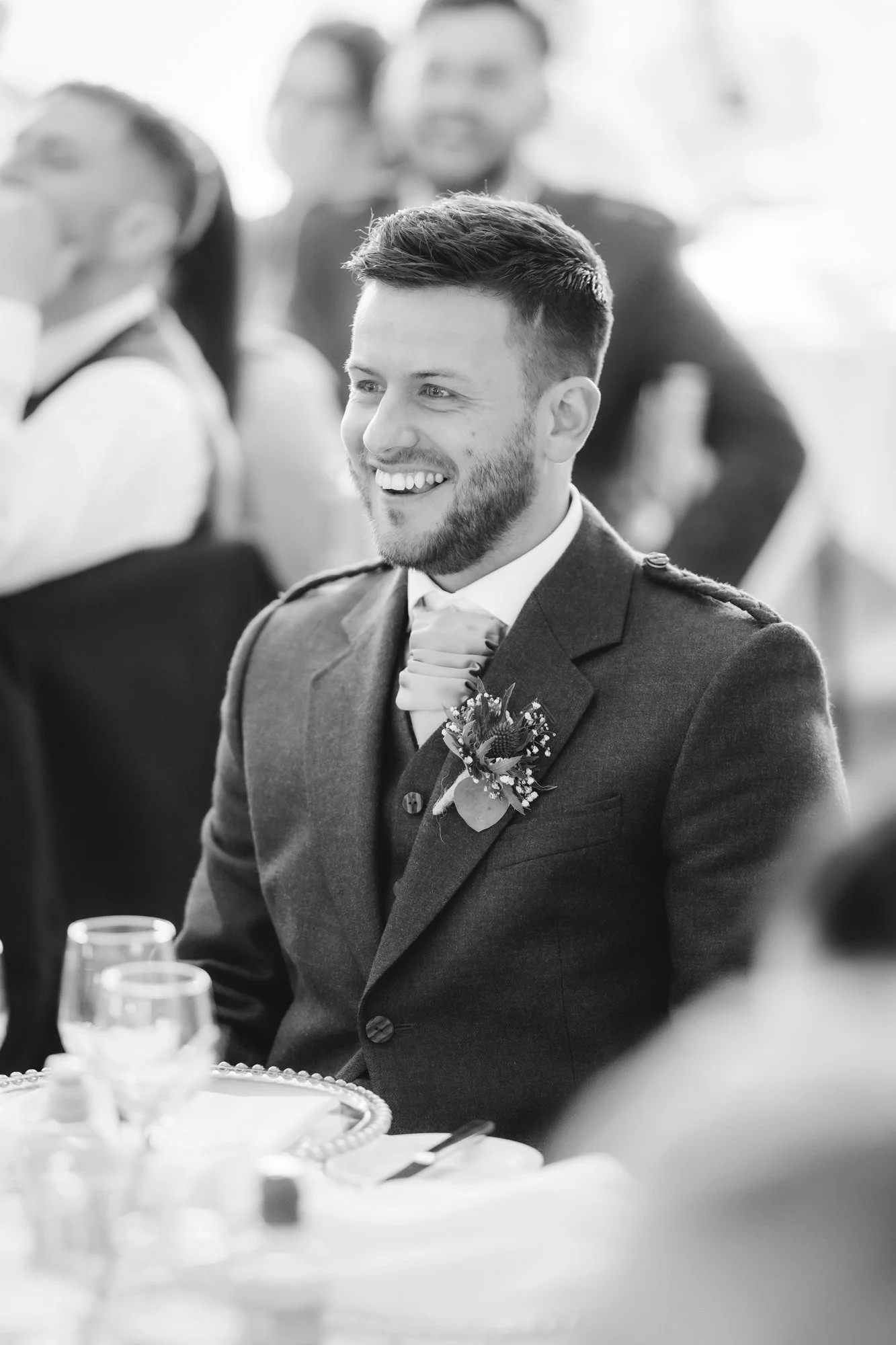 Black-and-white portrait of a guest in Highland dress smiling at the table at Glenbervie House.