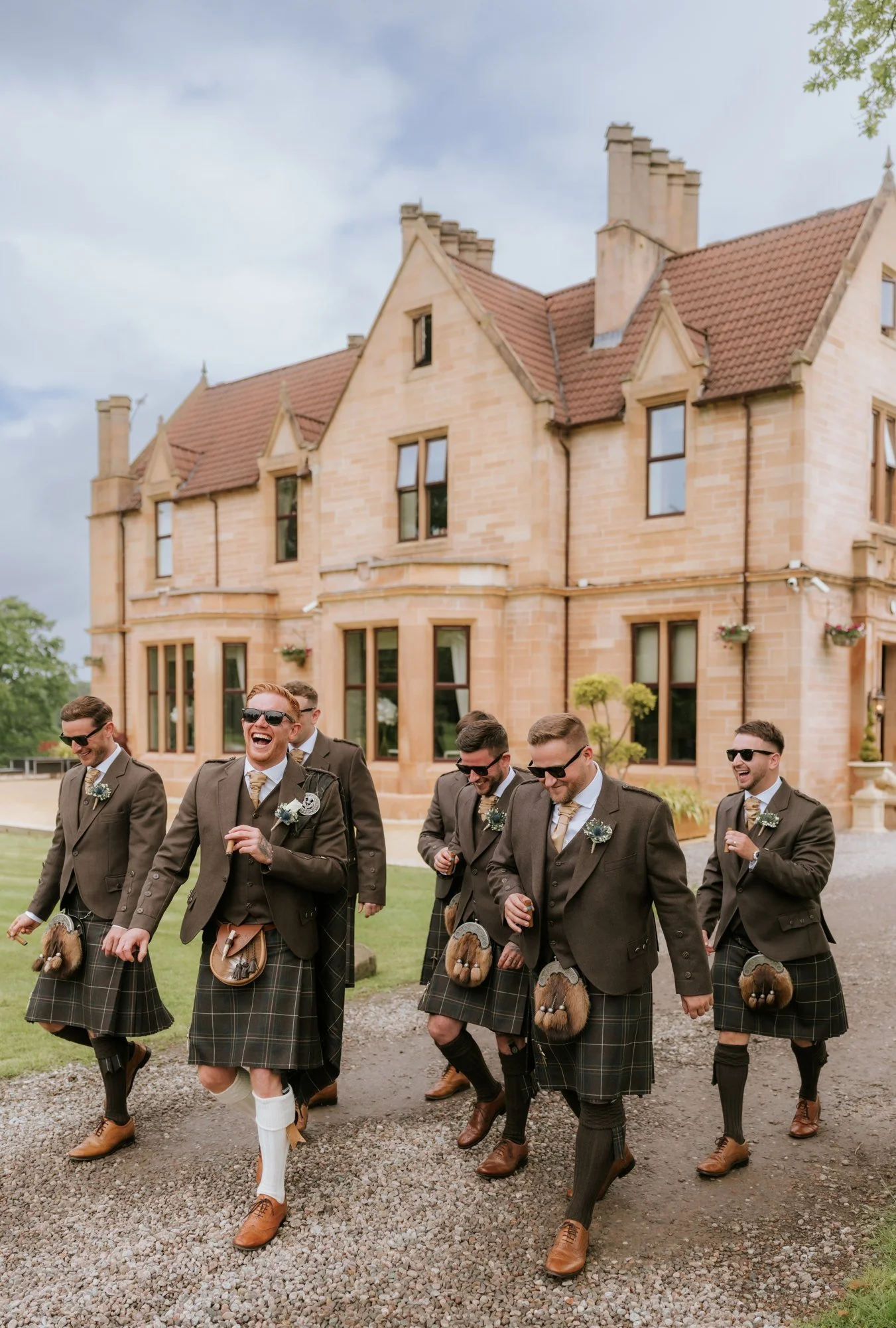 Scott and his groomsmen laughing outside Glenbervie House in matching kilts.