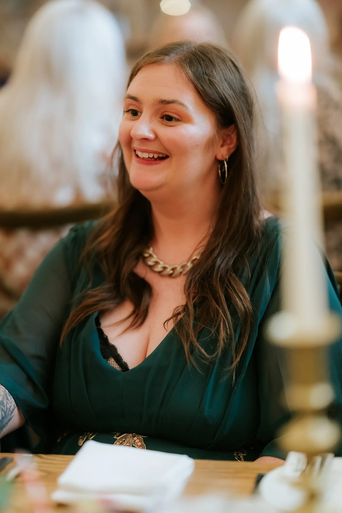 A guest in a dark green dress smiles during the speeches, framed by soft candlelight.