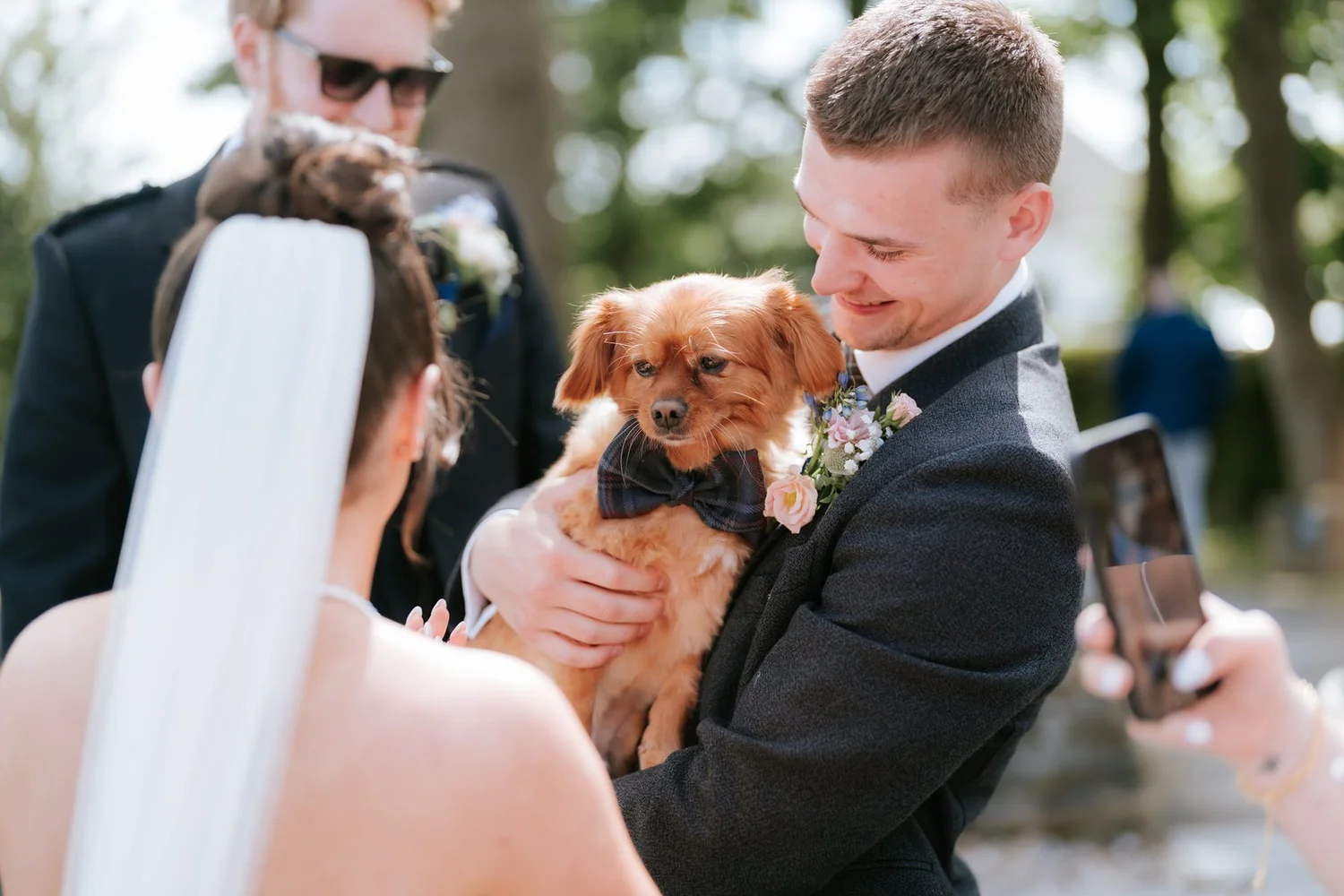 A wedding guest holding Lois and Dougie’s small dog while chatting to Lois outside.
