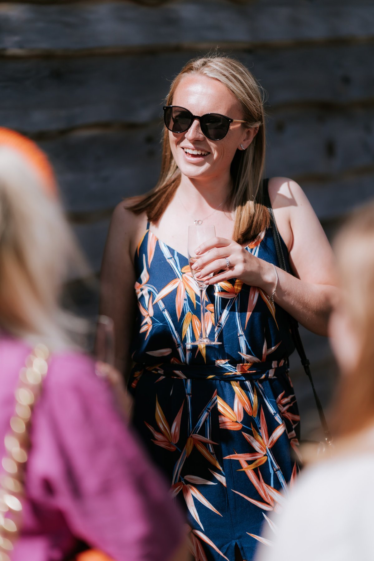 A guest in a floral dress and sunglasses smiling during the drinks reception.
