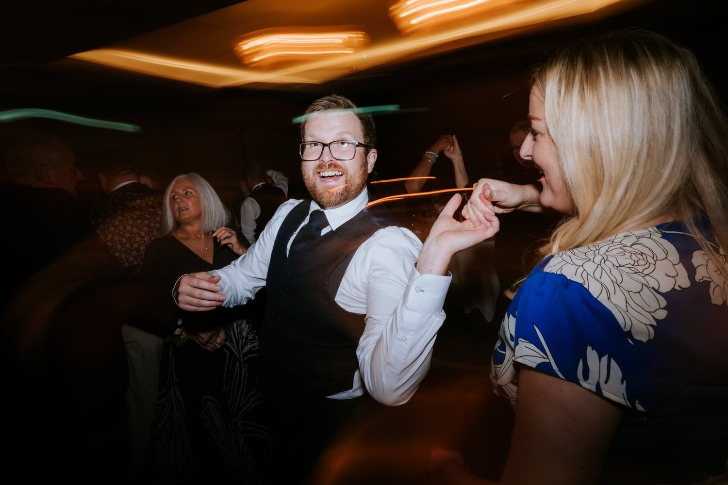 A guest in glasses and a waistcoat laughing on the wedding dance floor.