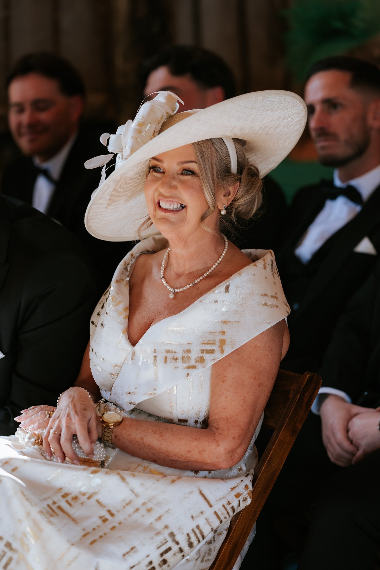 A wedding guest in a cream hat laughing