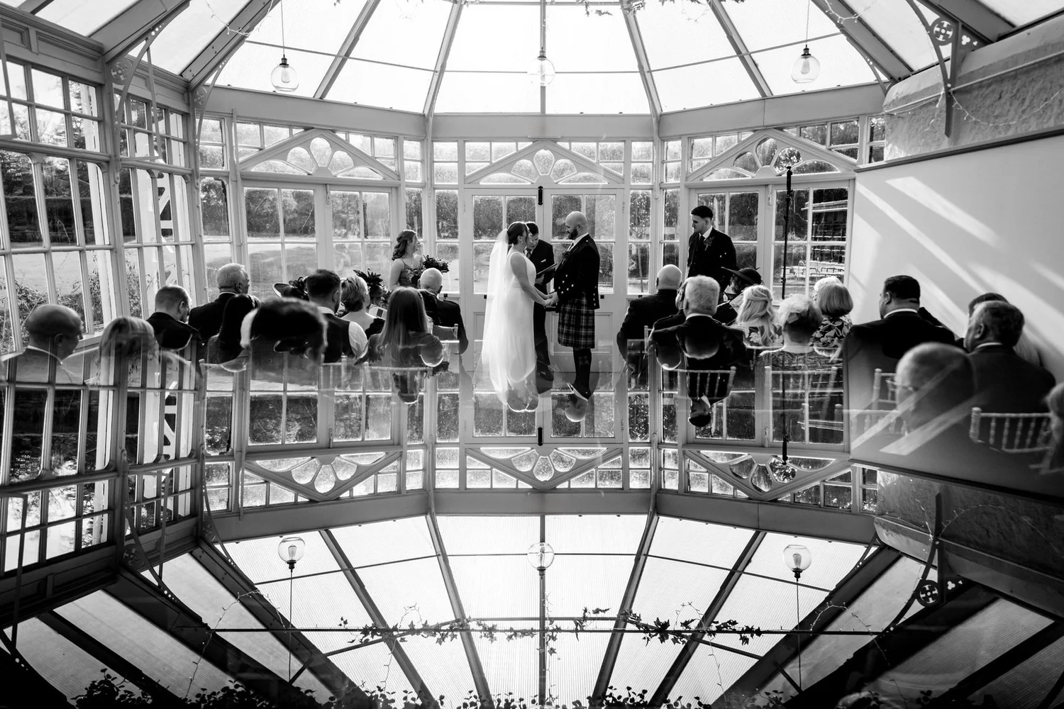 Black-and-white reflection of Kendall and Ewen’s conservatory ceremony in a grand piano.