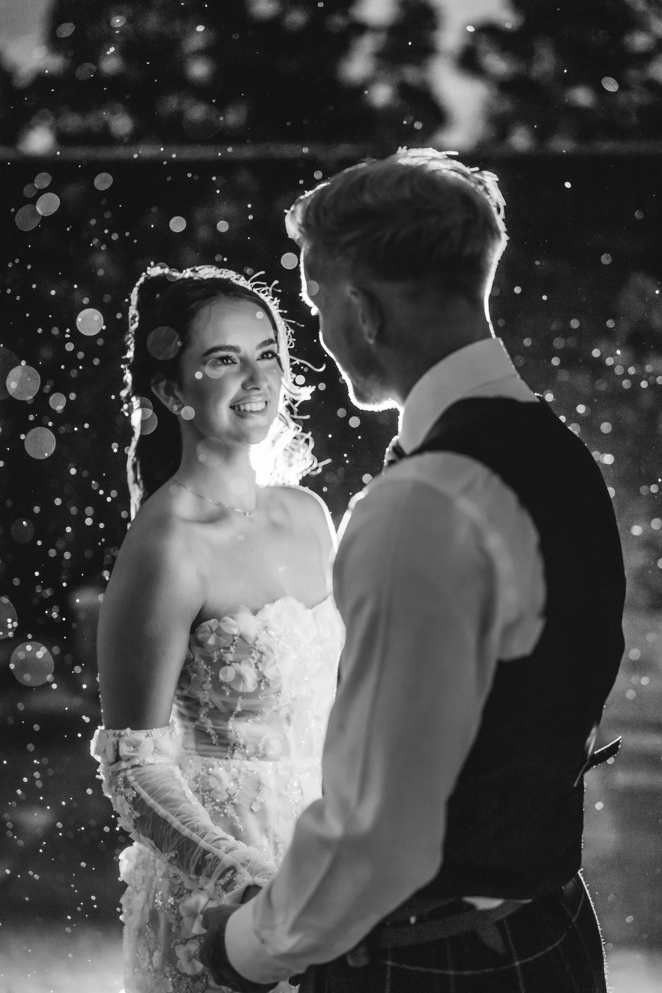 Black-and-white close-up of Kaitlyn smiling at Scott through backlit raindrops at Glenbervie House.