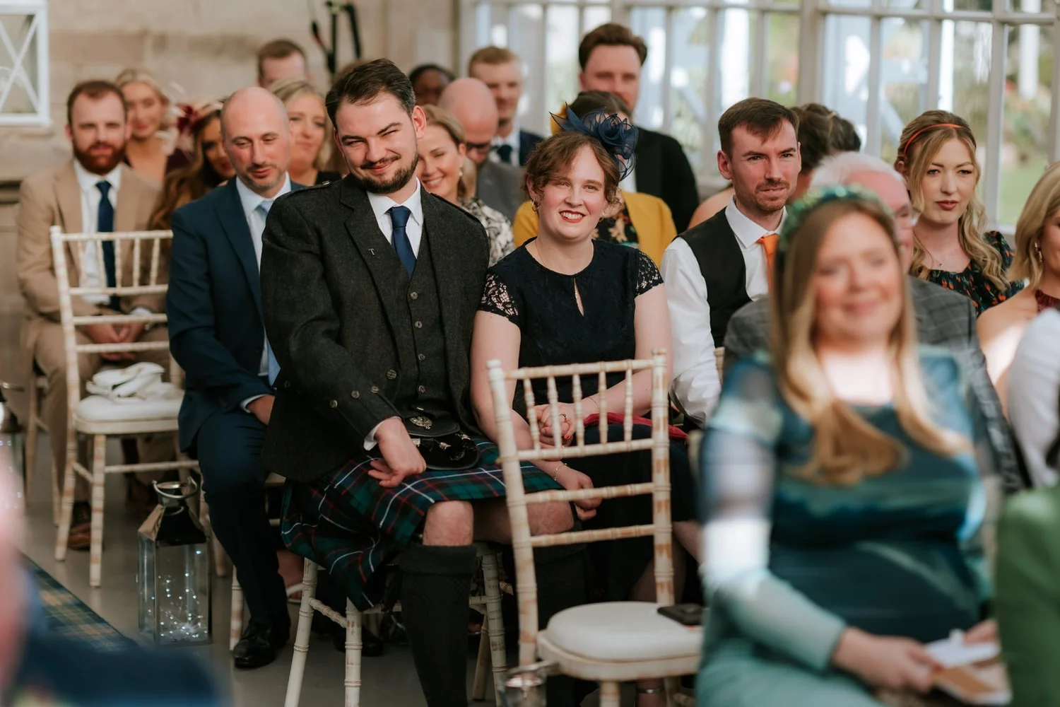 Wedding guests watching the ceremony from rows of chairs in the conservatory.
