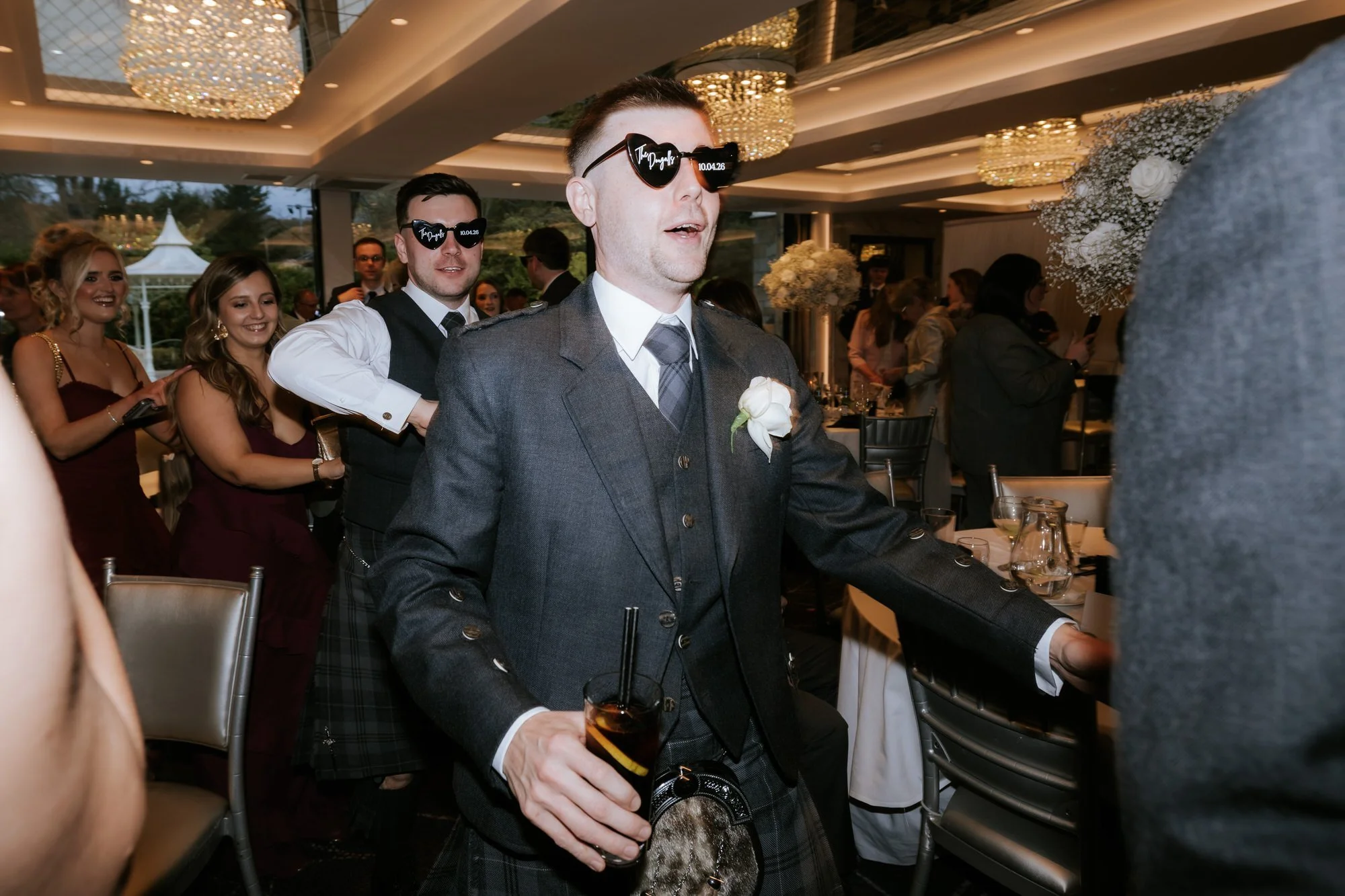 Wedding guests in heart-shaped sunglasses dancing in a conga line