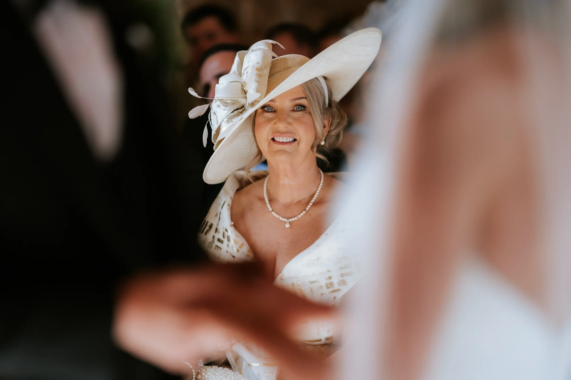 A guest in a cream hat smiling, framed between the couple