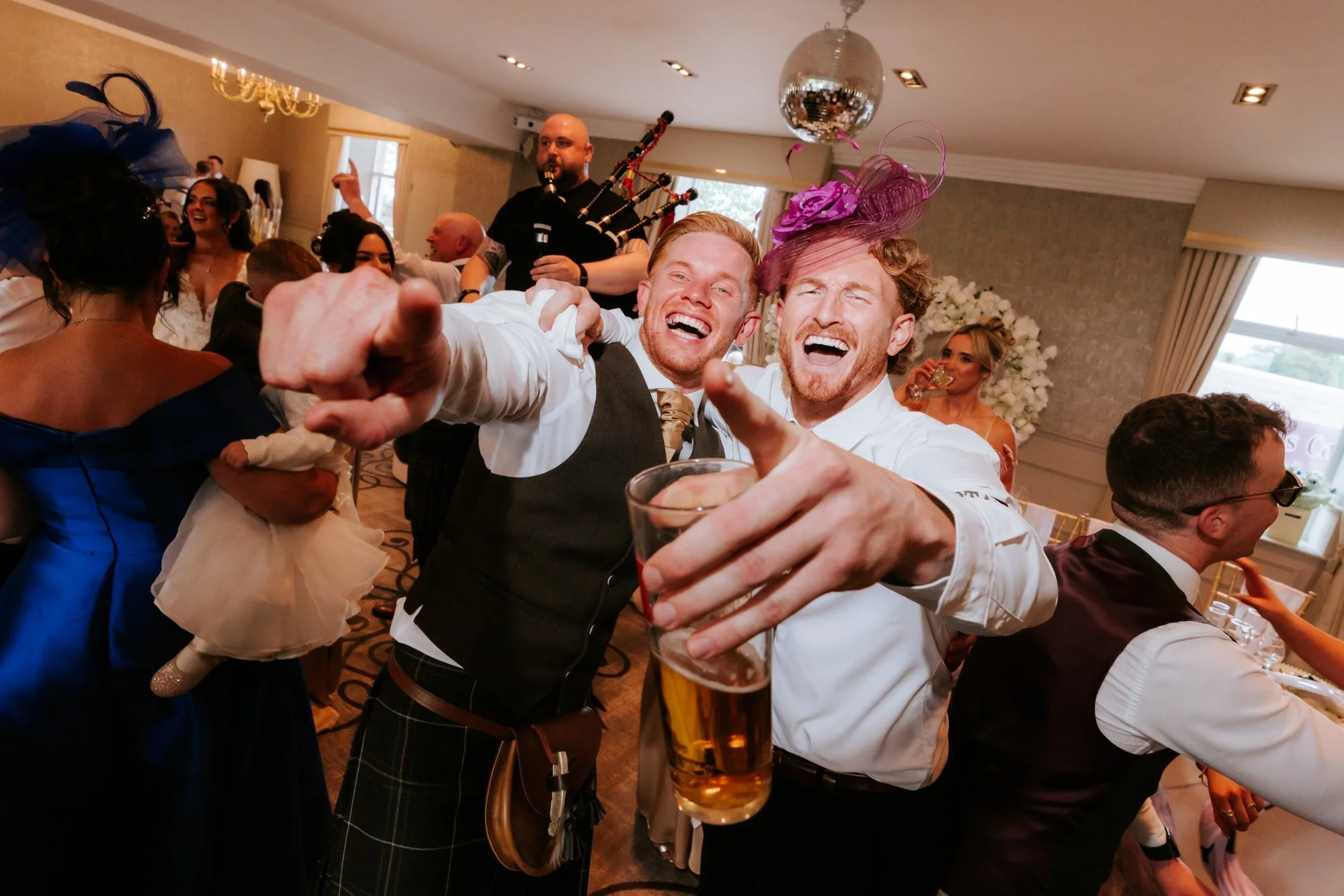 Scott and a guest wearing a pink fascinator laughing towards the camera at Glenbervie House.