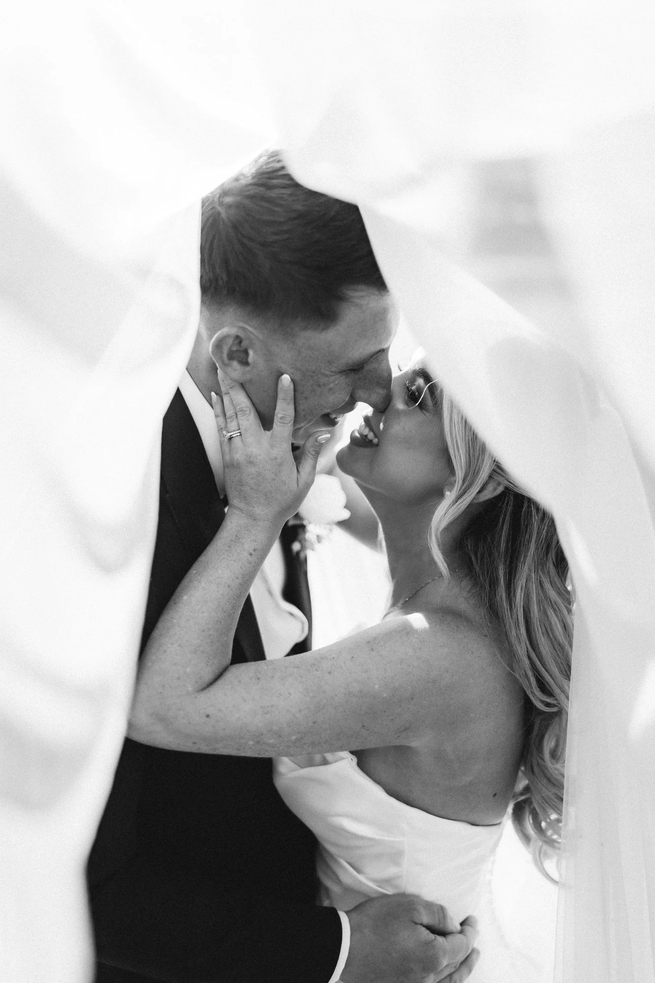 Aiden and Taylor sharing a kiss beneath the veil in black and white.