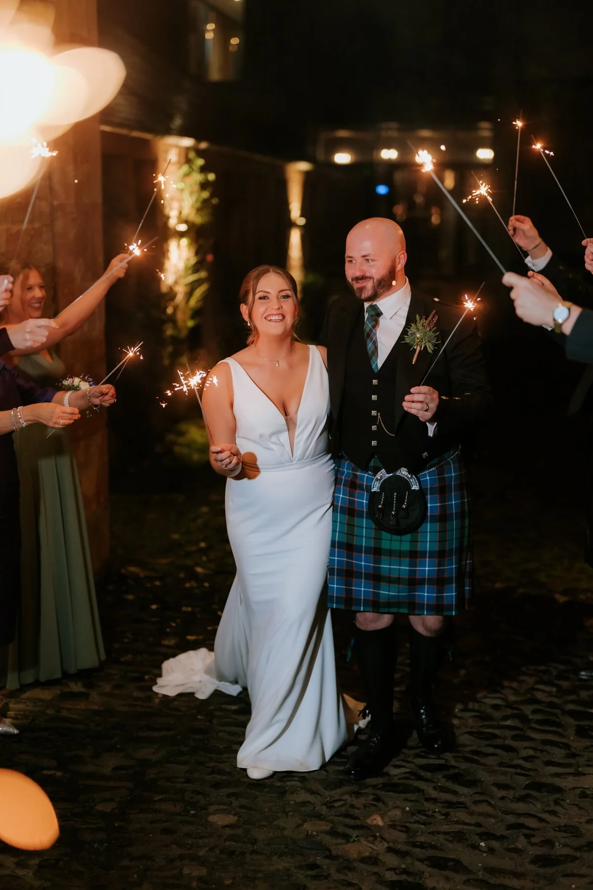 Kendall and Ewen walking between guests holding sparklers at night.