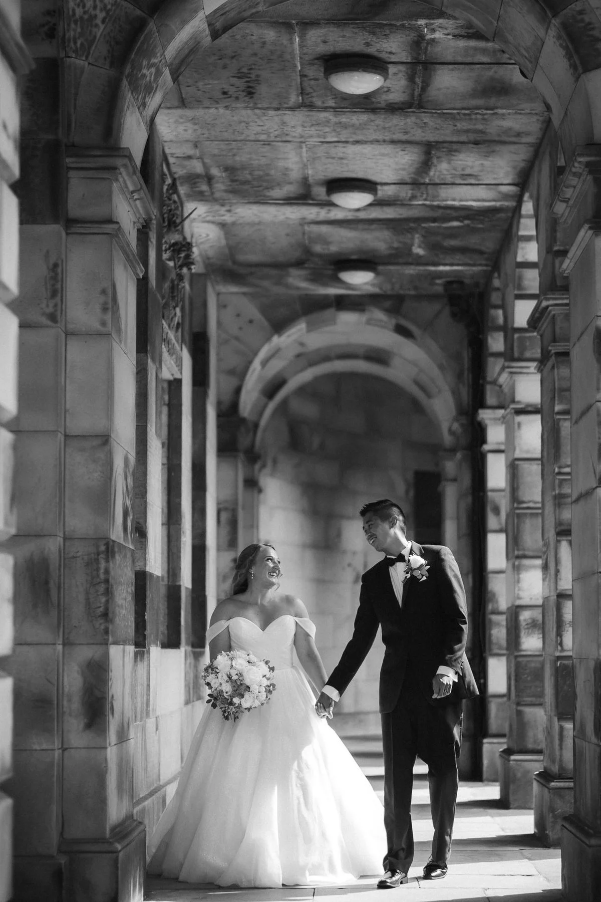 Allie and Carl walking beneath the stone arches of an Edinburgh Old Town arcade.